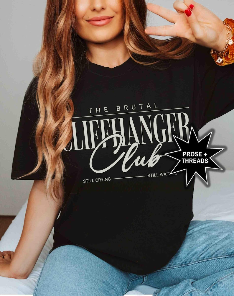 May include: Black t-shirt with white text that reads "The Brutal Cliffhanger Club" with the words "Still Crying" and "Still Waiting" underneath. A star with the words "Prose + Threads" is in the upper right corner.
