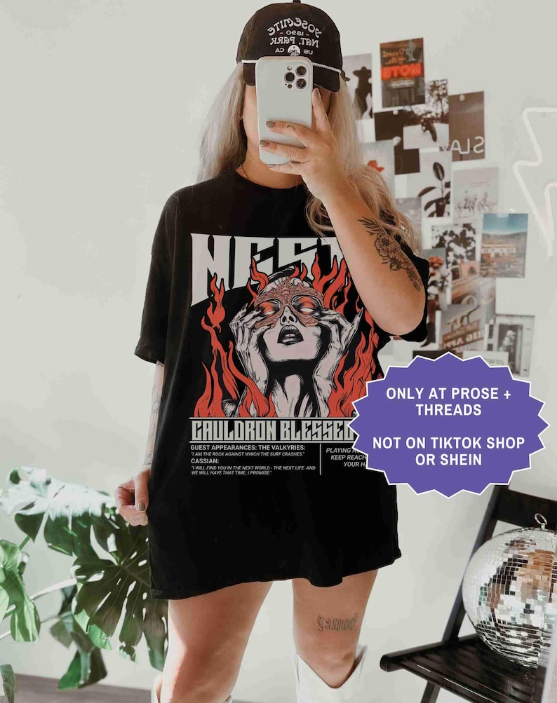 May include: Black t-shirt with a graphic of a woman's face surrounded by flames and the text "CAULDRON BLESSED". The shirt also has the text "ONLY AT PROSE + THREADS" and "NOT ON TIKTOK SHOP OR SHEIN".