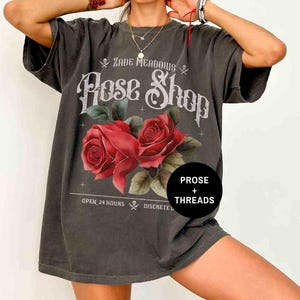 May include: A dark gray oversized t-shirt with a vintage-style graphic print of roses and the text "Zade Meadows Rose Shop" with the words "Prose + Threads" below. The text also says "Open 24 Hours Discrete"