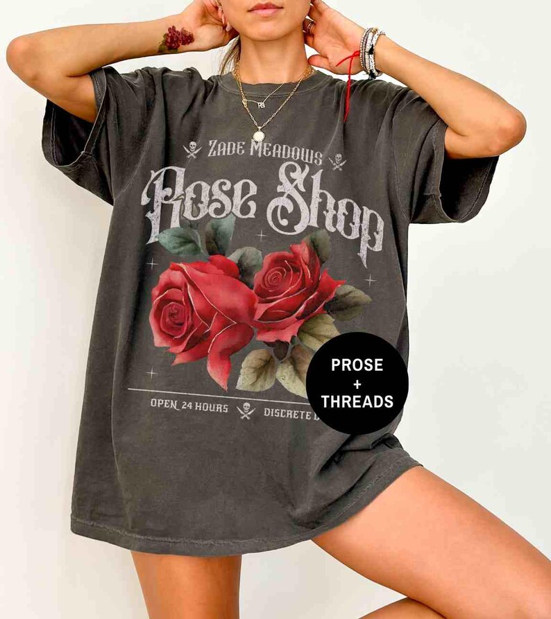 May include: A dark gray oversized t-shirt with a vintage-style graphic print of roses and the text "Zade Meadows Rose Shop" with the words "Prose + Threads" below. The text also says "Open 24 Hours Discrete"