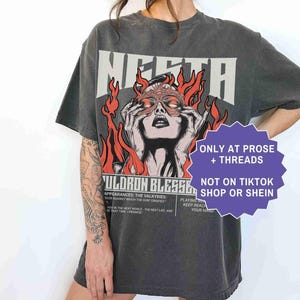 May include: Dark gray t-shirt with a graphic of a woman with a mask surrounded by flames, the word "MERTA" above her. Text on the shirt includes "ONLY AT PROSE + THREADS" and "NOT ON TIKTOK SHOP OR SHEIN". The word "PEPPER" is at the bottom.