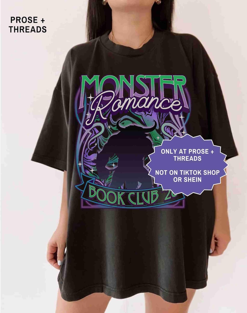 Op de afbeelding: Zwart T-shirt met een grafisch ontwerp met de tekst "MONSTER Romance BOOK CLUB 2". Het ontwerp bevat een silhouet van een wezen en decoratieve krullen in groen, paars en blauw. Het shirt heeft ook de tekst "ONLY AT PROSE + THREADS" en "NOT ON TIKTOK SHOP OR SHEIN".