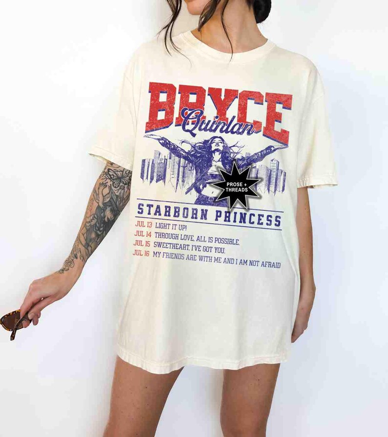 May include: An oversized cream-coloured t-shirt with a vintage-style graphic print featuring a woman with long dark hair, the text "Bryce Quinlan", and the words "Starborn Princess". The graphic also includes the text "Prose + Threads" and a list of dates and phrases.