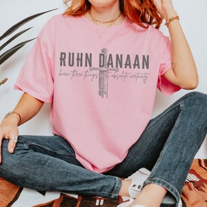May include: Pink t-shirt featuring a graphic of a sword and the text "RUHN DANAAN knew three things with absolute certainty".
