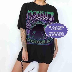 Op de afbeelding: Zwart T-shirt met de tekst "Monster Romance" in groen en paars, met een silhouet. Het shirt heeft ook "Book Club '26" en een paarse en witte afbeelding. Een paars en wit bord zegt "ONLY AT PROSE + THREADS NOT ON TIKTOK SHOP OR SHEIN".