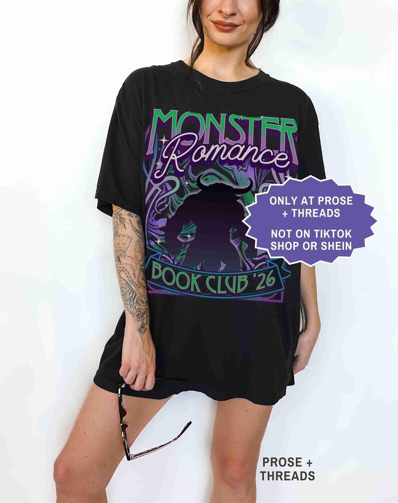 Op de afbeelding: Zwart T-shirt met de tekst "Monster Romance" in groen en paars, met een silhouet. Het shirt heeft ook "Book Club '26" en een paarse en witte afbeelding. Een paars en wit bord zegt "ONLY AT PROSE + THREADS NOT ON TIKTOK SHOP OR SHEIN".