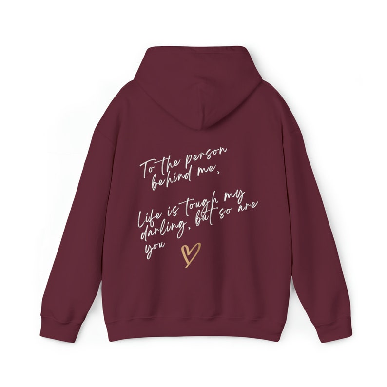May include: Burgundy hoodie with a hood and long sleeves. The back of the hoodie features the text "To the person behind me, Life is tough my darling, but so are you" with a gold heart symbol.