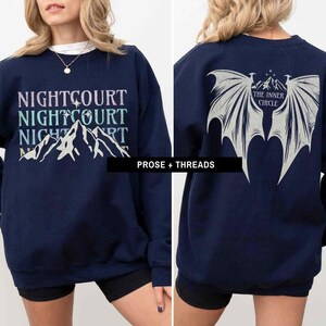 May include: A navy blue sweatshirt with a graphic of mountains and the text "NIGHTCOURT NIGHTCOURT NIGHTCOURT" on the front. The back of the sweatshirt has a graphic of wings with the text "THE INNER CIRCLE" in a circle.