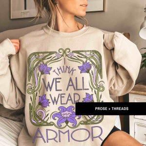 May include: A beige sweatshirt with a graphic print of a floral design and the text "I think we all wear armor".