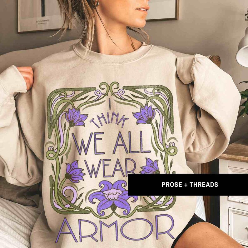 May include: A beige sweatshirt with a graphic print of a floral design and the text "I think we all wear armor".