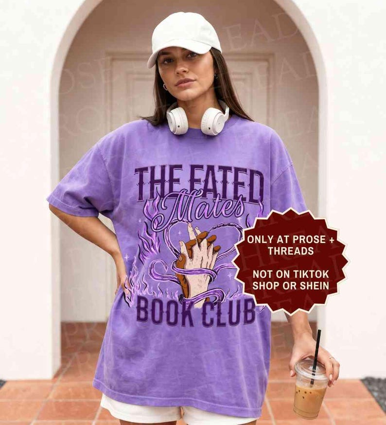 Pode incluir: Uma t-shirt roxa de manga curta com o texto THE FATED MATES BOOK CLUB e um gr&aacute;fico de duas m&atilde;os entrela&ccedil;adas em forma de cora&ccedil;&atilde;o rodeadas por chamas roxas. A t-shirt inclui um bon&eacute; de basebol branco e auscultadores brancos.