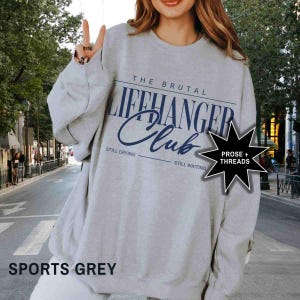 Puede incluir: Una sudadera gris con el texto "The Brutal Lifehanger Club" en azul. El texto "Still Crying" y "Still Waiting" est&aacute; impreso debajo del texto principal. Una estrella negra con el texto "Prose + Threads" est&aacute; en la esquina inferior derecha. La sudadera est&aacute; etiquetada como "Sports Grey".