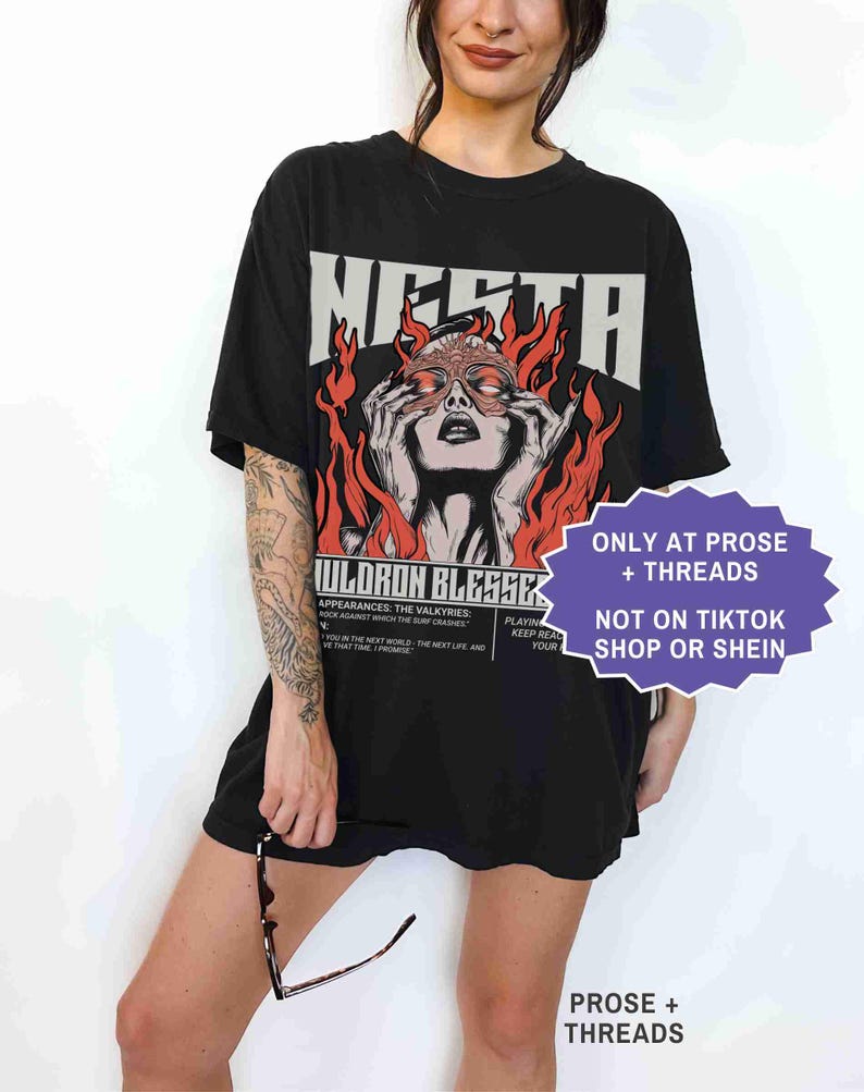 May include: Black oversized t-shirt with a graphic featuring the word "MERTA" above an illustration of a woman with flames. Text on the shirt includes "JULDRON BLESSEK" and other phrases. A purple sticker reads "ONLY AT PROSE + THREADS NOT ON TIKTOK SHOP OR SHEIN."