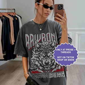 Op de afbeelding: Donkergrijs t-shirt met een wolfafbeelding en het woord "RAWRON" in wit. Het shirt heeft ook de tekst "ONLY AT PROSE + THREADS" en "NOT ON TIKTOK SHOP OR SHEIN".