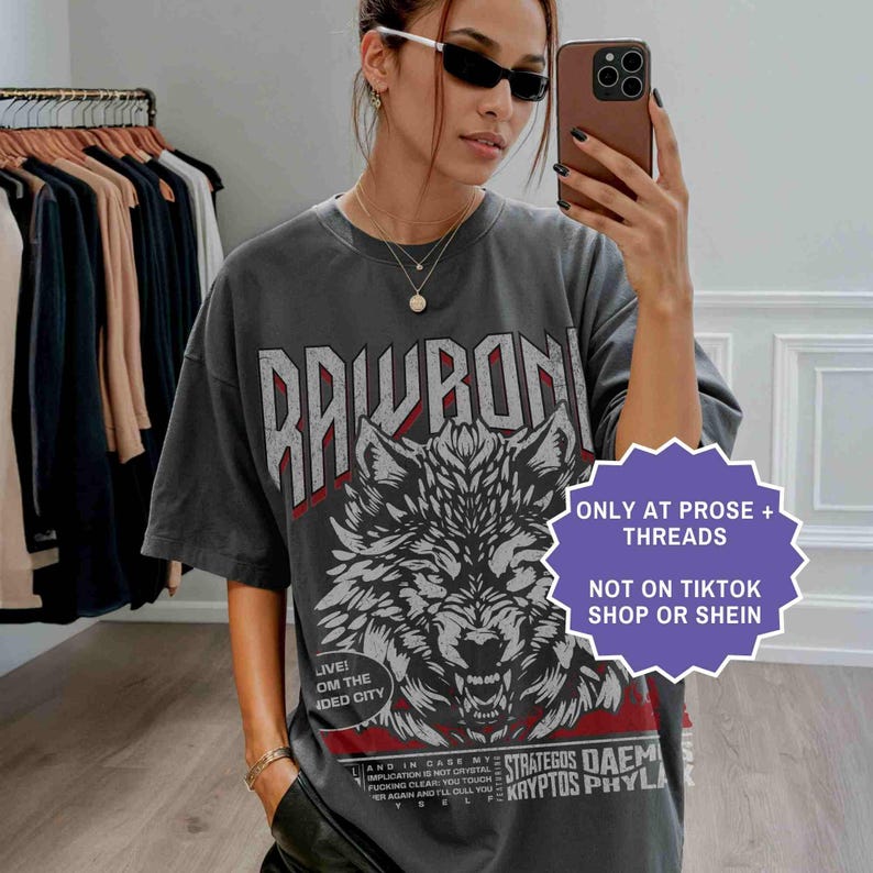 Op de afbeelding: Donkergrijs t-shirt met een wolfafbeelding en het woord "RAWRON" in wit. Het shirt heeft ook de tekst "ONLY AT PROSE + THREADS" en "NOT ON TIKTOK SHOP OR SHEIN".