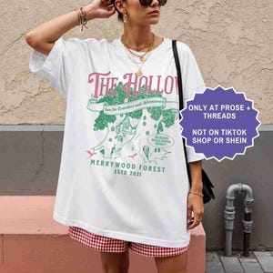 Pu&ograve; includere: T-shirt bianca con una grafica che raffigura la locanda "The Hollow", un design di casa sull'albero e la scritta "Merrywood Forest ESTD 2021". La maglietta ha anche un'etichetta viola con la scritta "ONLY AT PROSE + THREADS NOT ON TIKTOK SHOP OR SHEIN."
