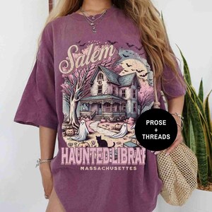 May include: Purple oversized t-shirt with a graphic print of a haunted house in Salem, Massachusetts. The graphic also includes the text "Salem Haunted Library".