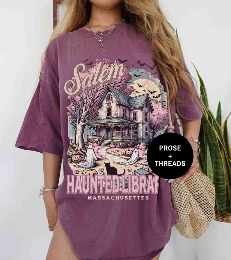 May include: Purple oversized t-shirt with a graphic print of a haunted house in Salem, Massachusetts. The graphic also includes the text "Salem Haunted Library".
