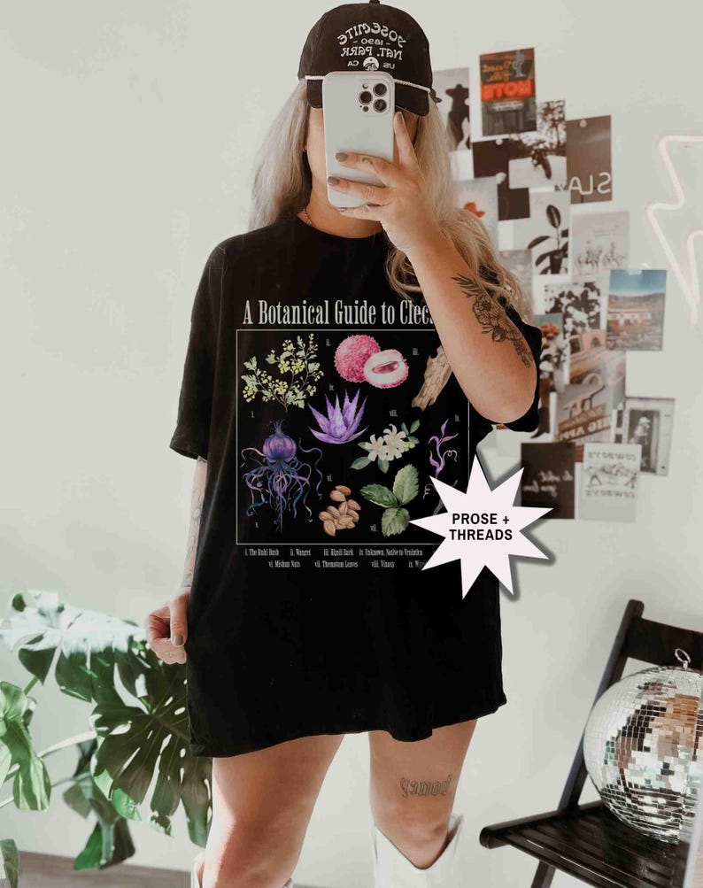 May include: Black t-shirt with a botanical illustration and the text "A Botanical Guide to Clec." The illustration features various plants and flowers, including a lychee, a jellyfish, and a flower with purple petals. The text "PROSE + THREADS" is in a white starburst.