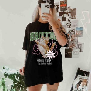 May include: Black oversized t-shirt with a graphic of a cat in a green and white "BROCCO" design. The text "PROSE + THREADS" and "Nobody Wants it But It's Good For You!" is printed on the shirt.