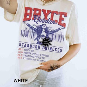 May include: White t-shirt featuring a graphic print of a woman in a city skyline. The text "Bryce Quinlan" is printed in red and blue. The text "Starborn Princess" is printed in blue. The text "Prose + Threads" is printed in black.