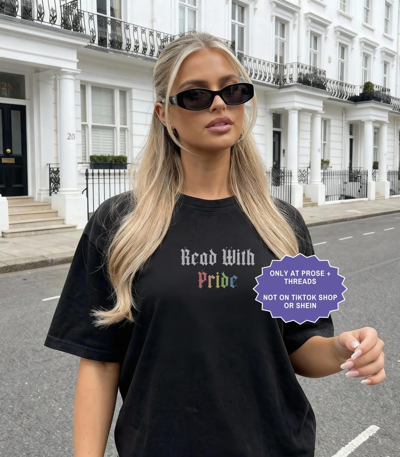 Pu&ograve; includere: Una t-shirt nera a maniche corte con il testo Read With Pride in un carattere gotico, con la parola Pride visualizzata nei colori dell'arcobaleno. Un grafico viola a forma di stella include il testo ONLY AT PROSE + THREADS NOT ON TIKTOK SHOP OR SHEIN.