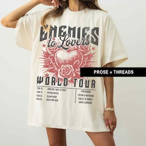 Pode incluir: Uma camiseta bege com uma estampa gr&aacute;fica de um cora&ccedil;&atilde;o com rosas e o texto "Enemies to Lovers World Tour". O gr&aacute;fico &eacute; em preto e vermelho. O texto abaixo do gr&aacute;fico lista as datas da turn&ecirc; e os destaques.