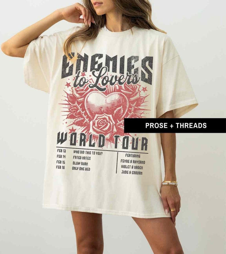 Pode incluir: Uma camiseta bege com uma estampa gr&aacute;fica de um cora&ccedil;&atilde;o com rosas e o texto "Enemies to Lovers World Tour". O gr&aacute;fico &eacute; em preto e vermelho. O texto abaixo do gr&aacute;fico lista as datas da turn&ecirc; e os destaques.