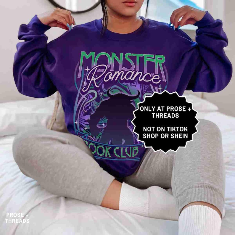 May include: A purple crewneck sweatshirt with the words "MONSTER Romance BOOK CLUB" in a stylized design. The graphic includes a silhouette of a horned figure. The sweatshirt has long sleeves.