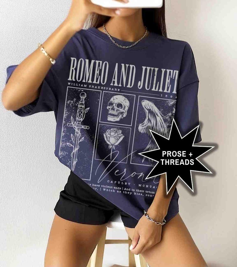 May include: Navy blue t-shirt featuring a graphic design from Shakespeare's Romeo and Juliet. The design includes a sword, skull, rose, and angel wing. The text "ROMEO AND JULIET" and "Verona" are also visible.