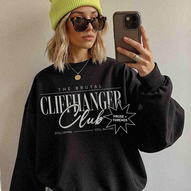 Puede incluir: Sudadera negra con texto blanco que dice "The Brutal Cliffhanger Club" con una estrella y el texto "Prose + Threads" debajo. El texto "Still Crying" y "Still Waiting" est&aacute;n debajo de la estrella.