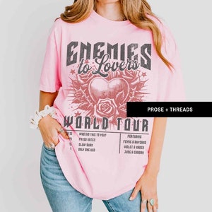 Pode incluir: Camiseta rosa com uma estampa gr&aacute;fica de um cora&ccedil;&atilde;o com espinhos e o texto "Enemies to Lovers World Tour" com uma lista de t&iacute;tulos de m&uacute;sicas e artistas. O texto "Prose + Threads" est&aacute; no canto superior direito.