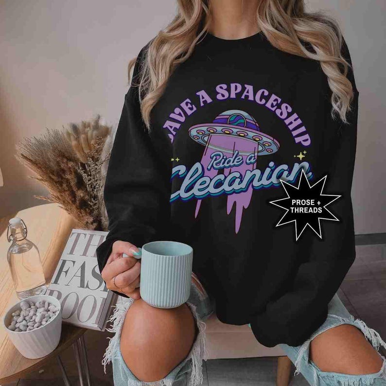 May include: A black sweatshirt with a purple and blue graphic of a spaceship with the text "Save a Spaceship Ride a Lecanian" and a small starburst logo with the text "Prose + Threads".