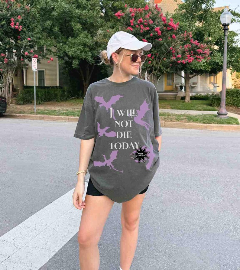 May include: A dark gray oversized t-shirt with a purple graphic of dragons and the text "I will not die today".