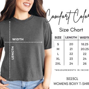 May include: A dark gray Comfort Colors boxy t-shirt with a size chart. The size chart shows measurements in inches for sizes S to 2XL. The shirt is labeled as 3023CL Womens Boxy T-Shirt.
