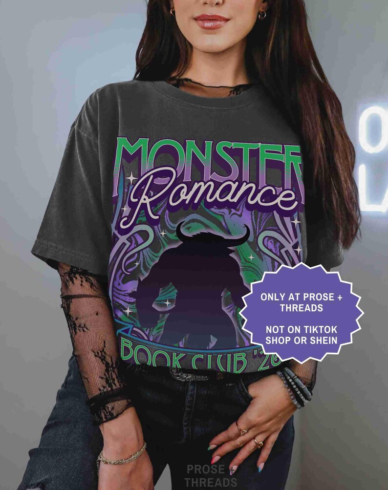 Op de afbeelding: Donkergrijs t-shirt met de woorden "Monster Romance Book Club '20" in groen en paars. De afbeelding toont een monstersilhouet. Een paars en wit label leest "ONLY AT PROSE + THREADS NOT ON TIKTOK SHOP OR SHEIN."