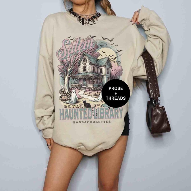 May include: A beige sweatshirt with a graphic print of a house with the text "Salem Haunted Library Massachusetts" and the words "Prose + Threads" in a circle.