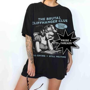 May include: Black t-shirt with the text "THE BRUTAL CLIFFHANGER CLUE" in light blue. The shirt features a black and white illustration of a crying woman reading a book. The text "LL CRYING - STILL WAITING" is also printed on the shirt.