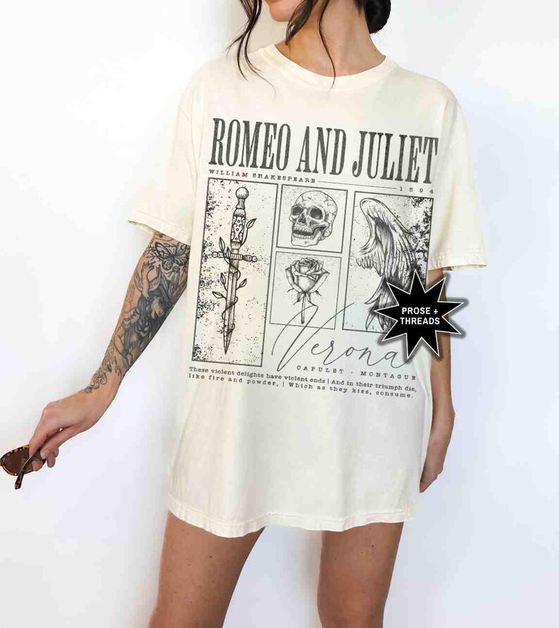 May include: Cream-colored t-shirt featuring a graphic design inspired by Shakespeare's "Romeo and Juliet." The design includes a sword, skull, rose, and a winged figure, with the text "Romeo and Juliet" and "Verona."