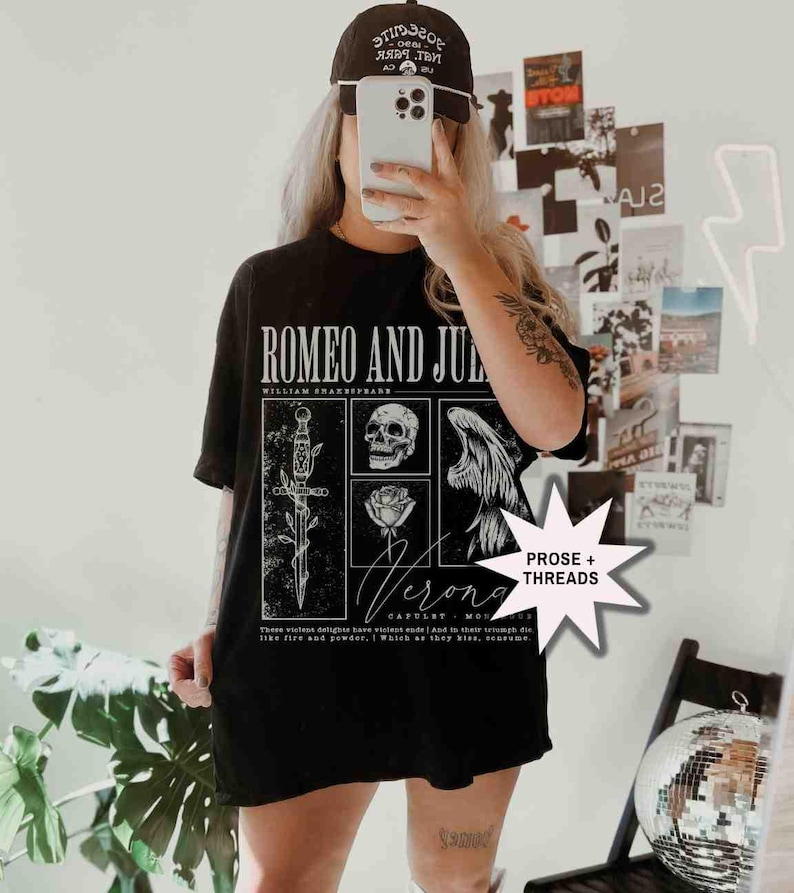 May include: Black t-shirt featuring a graphic design from Shakespeare's "Romeo and Juliet." The design includes a sword, skull, rose, and angel wings. The text "Verona" and a quote are also visible.