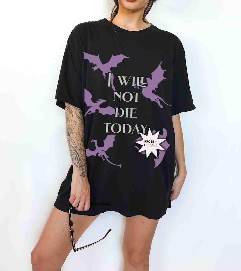 May include: Black oversized t-shirt with a purple graphic of dragons and the text "I will not die today". The shirt has a small purple tag with the text "Prose + Threads".