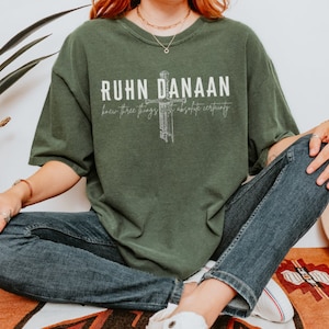 May include: A green t-shirt with a white graphic design featuring a cross and the text "RUHN DANAAN knew three things with absolute certainty".