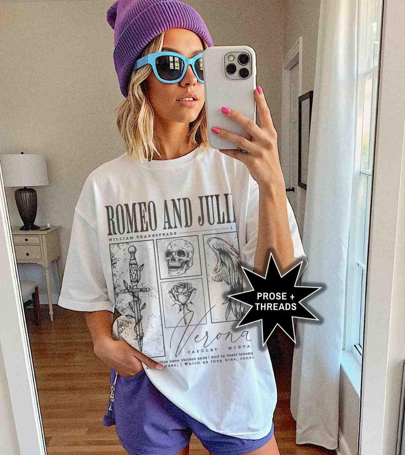 May include: White t-shirt with the text "ROMEO AND JULI" and illustrations of a sword, skull, angel wing, and rose. The shirt also has the word "Verona" printed on it. The person is wearing a purple beanie, blue sunglasses, and purple shorts.
