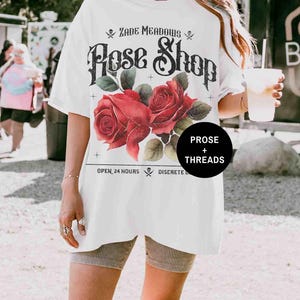 May include: White oversized t-shirt with a vintage graphic design featuring red roses and the text "Zade Meadows Rose Shop", "Open 24 Hours", "Discrete Delivery", and "Prose + Threads".