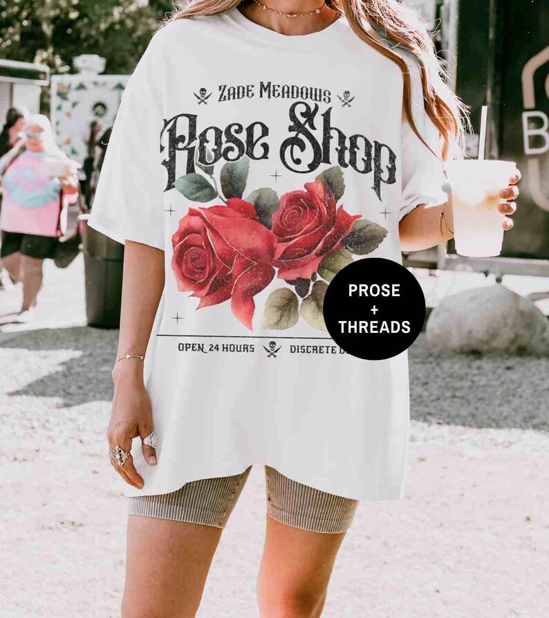 May include: White oversized t-shirt with a vintage graphic design featuring red roses and the text "Zade Meadows Rose Shop", "Open 24 Hours", "Discrete Delivery", and "Prose + Threads".