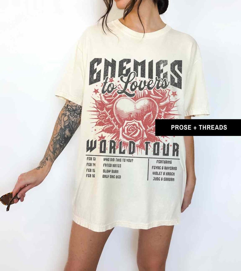 Pode incluir: Uma camiseta bege com uma estampa gr&aacute;fica preta e vermelha que diz "Enemies to Lovers World Tour". O gr&aacute;fico apresenta um cora&ccedil;&atilde;o com uma rosa e espinhos. A camiseta tamb&eacute;m lista as datas da turn&ecirc; e os artistas.