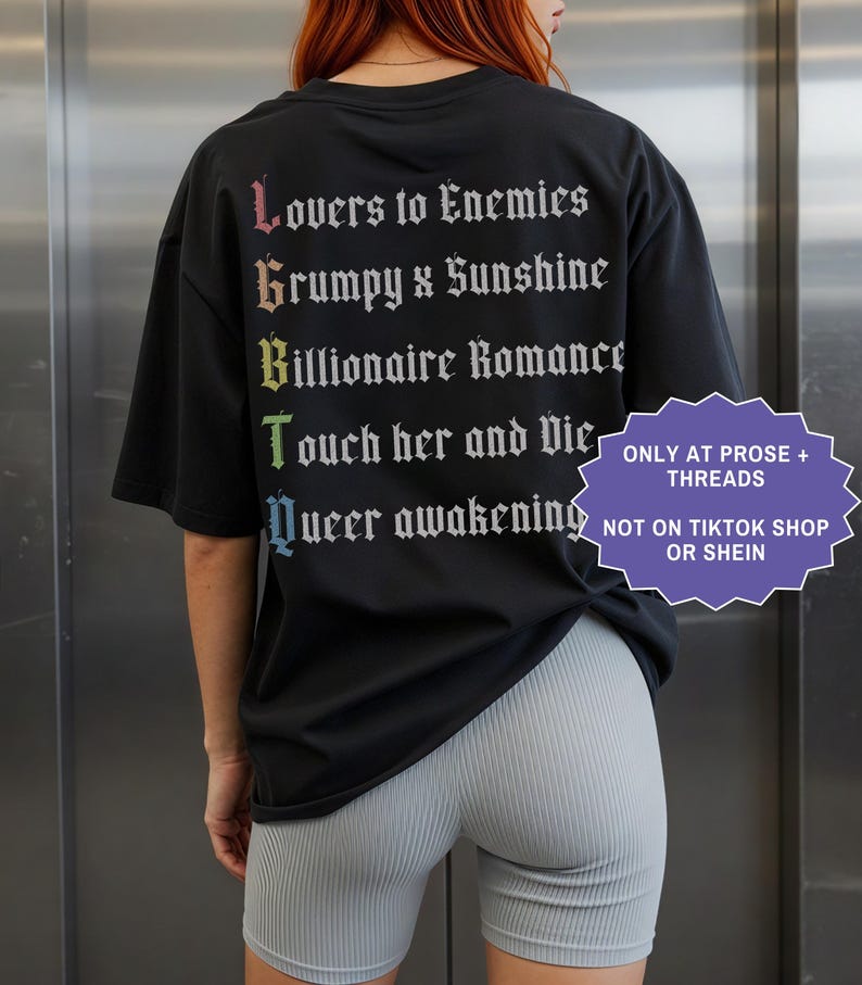 Pu&ograve; includere: Una t-shirt nera con testo bianco in carattere gotico sul retro, che elenca tropi letterari: Lovers to Enemies, Grumpy x Sunshine, Billionaire Romance, Touch her and Die e Queer awakening, con le lettere iniziali in un gradiente arcobaleno.