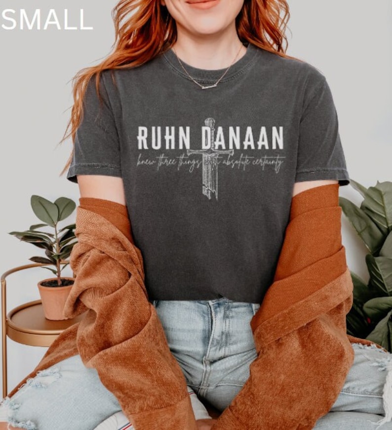 May include: A dark grey t-shirt with a white graphic design that says "RUHN DANAAN knew three things with absolute certainty". The graphic design features a stylised cross.