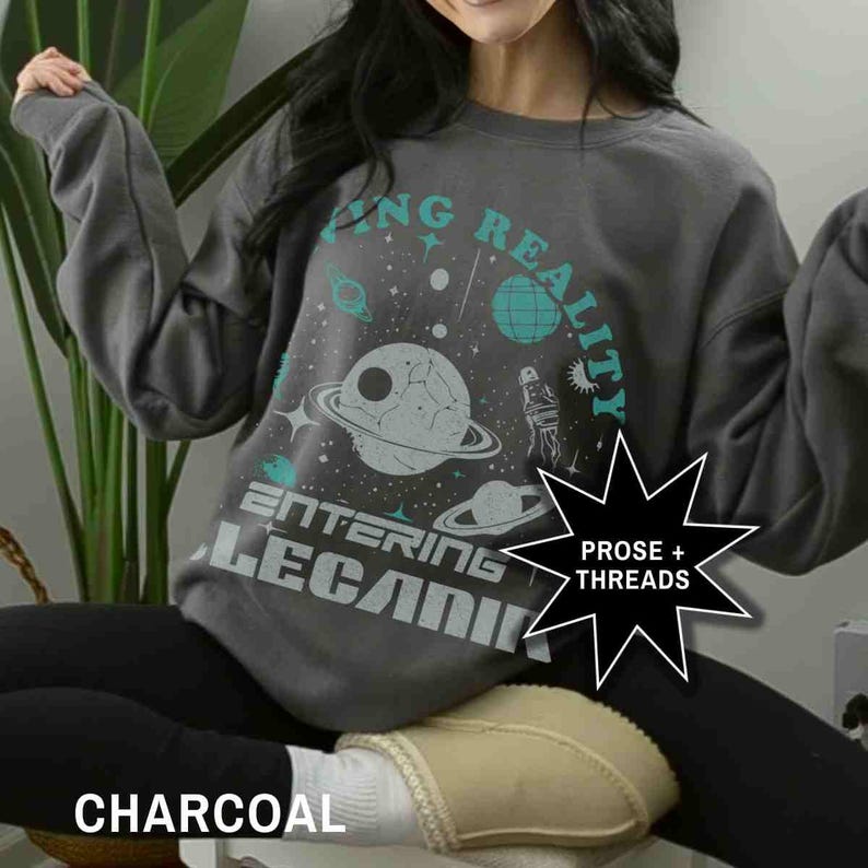 May include: A charcoal gray sweatshirt with a graphic print of planets, stars, and the text "Entering Reality". The text "Prose + Threads" is also printed on the sweatshirt.