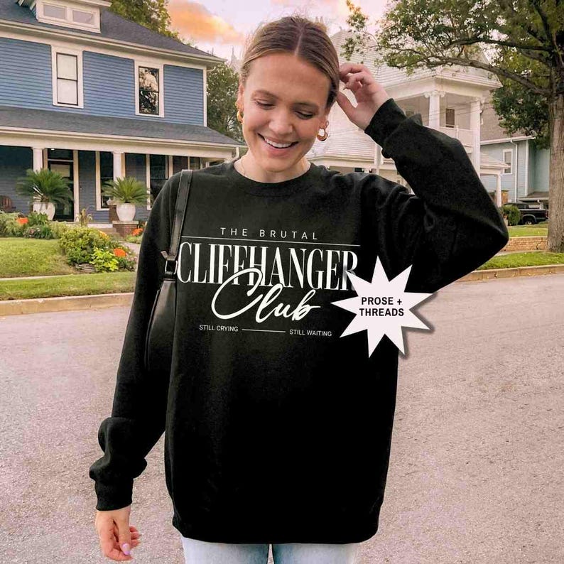 Puede incluir: Sudadera negra con texto blanco que dice "The Brutal Cliffhanger Club" con las palabras "Still Crying" y "Still Waiting" debajo del texto. Una estrella blanca con el texto "Prose + Threads" est&aacute; en la esquina superior derecha.